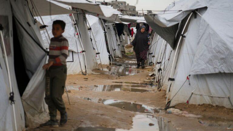 Une femme palestinienne porte un seau boueux alors qu'elle marche entre les tentes d'un vaste camp adjacent aux maisons et bâtiments détruits de la ville de Gaza City, dans la bande de Gaza, le samedi 1er mars 2025, pendant le mois du ramadan. (Keystone / AP Photo/Abdel Kareem Hana)